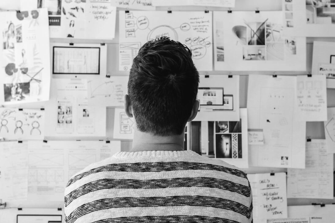 Man Wearing Black and White Stripe Shirt Looking at White Printer Papers on the Wall